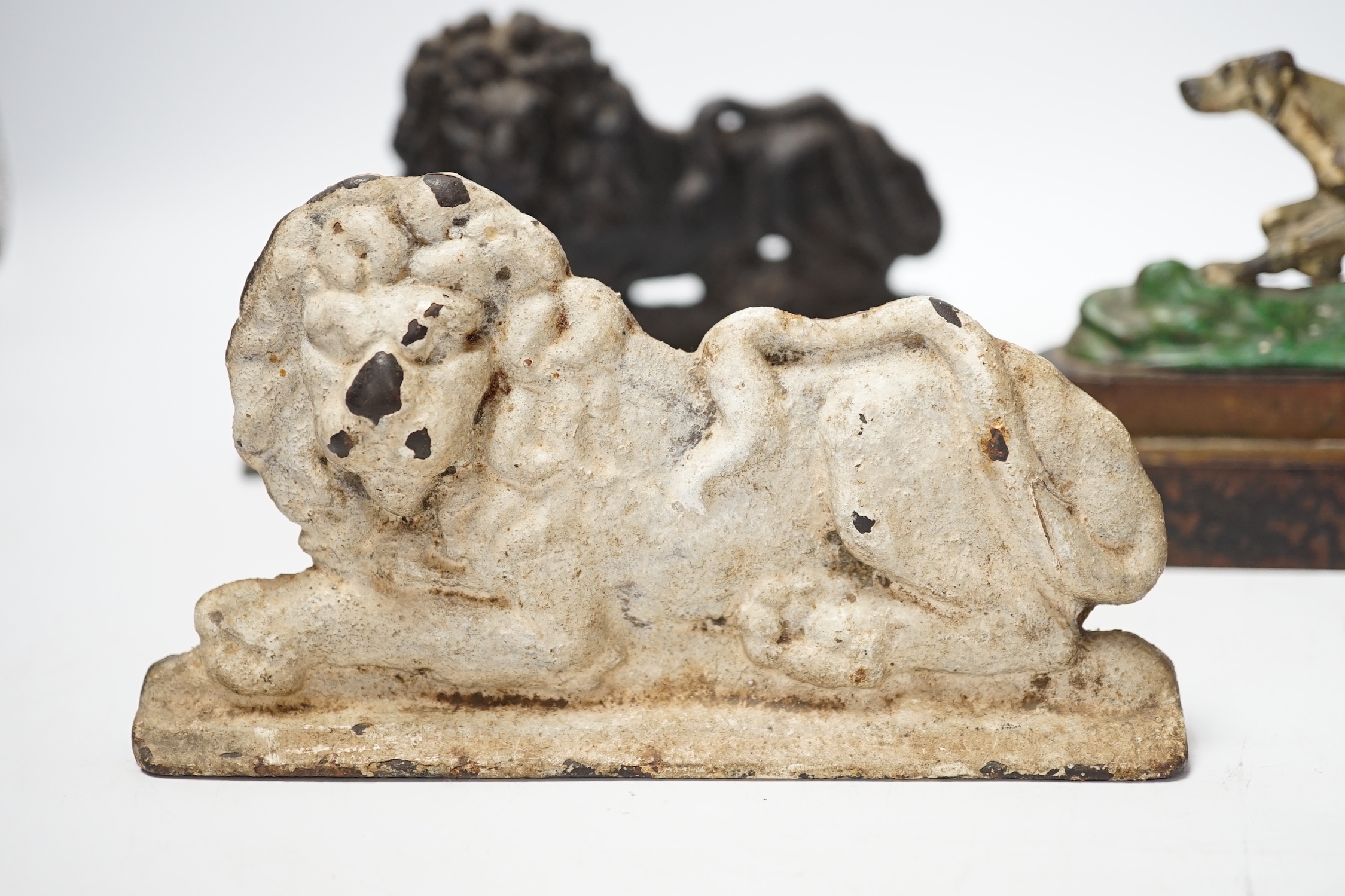 Two cast iron lion door stops and a painted dog door stop, 21cm wide